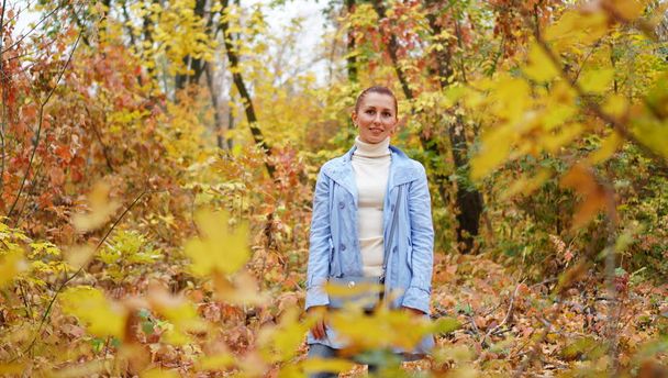 Happy women in a blue jacket enjoying autumn day in the park. The mood of autumn, leaf fall. - Фото, зображення