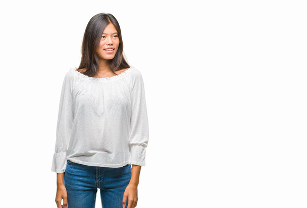 Jonge Aziatische vrouw over geïsoleerde achtergrond op zoek weg aan kant met glimlach op het gezicht, natuurlijke wijze van uitdrukking. Lachen vertrouwen. - Foto, afbeelding