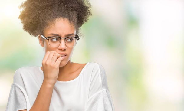 Stresli ve gergin elle çivi ısırma ağzına bakarak izole arka plan üzerinde gözlük takan genç afro Amerikalı kadın. Anksiyete sorunu. - Fotoğraf, Görsel