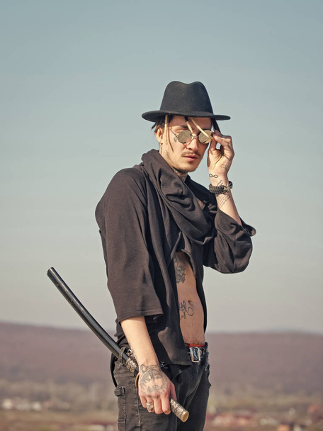 Warrior in sunglasses, black hat, tattooed torso in open clothes - Fotó, kép