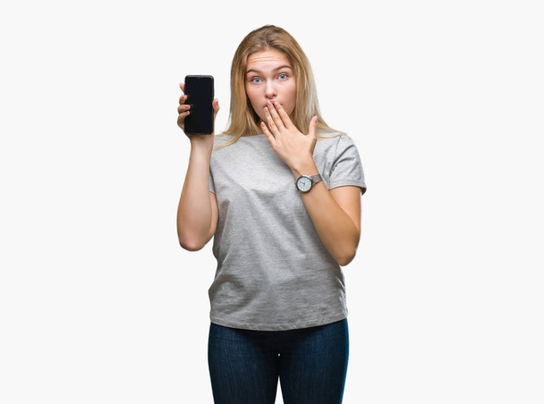 Young caucasian woman showing screen of smartphone over isolated background cover mouth with hand shocked with shame for mistake, expression of fear, scared in silence, secret concept - Valokuva, kuva
