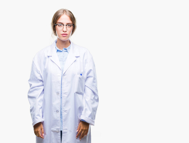Linda jovem mulher médica loira vestindo casaco branco sobre fundo isolado com expressão séria no rosto. Simples e natural olhando para a câmera
. - Foto, Imagem