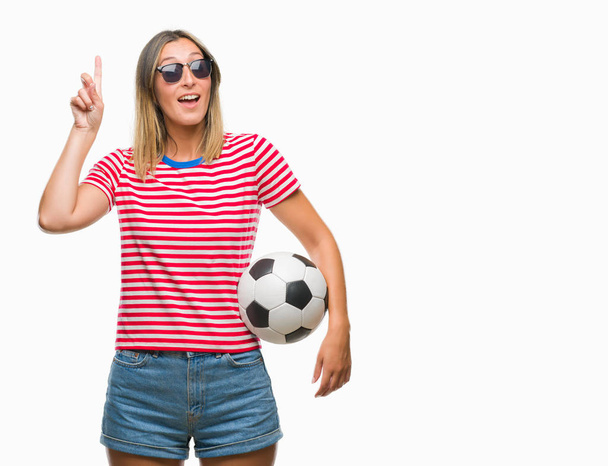Young beautiful woman holding soccer football ball over isolated background surprised with an idea or question pointing finger with happy face, number one - Фото, зображення