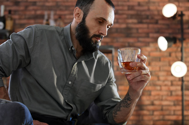 Handsome man holding glass of whiskey indoors - Foto, afbeelding