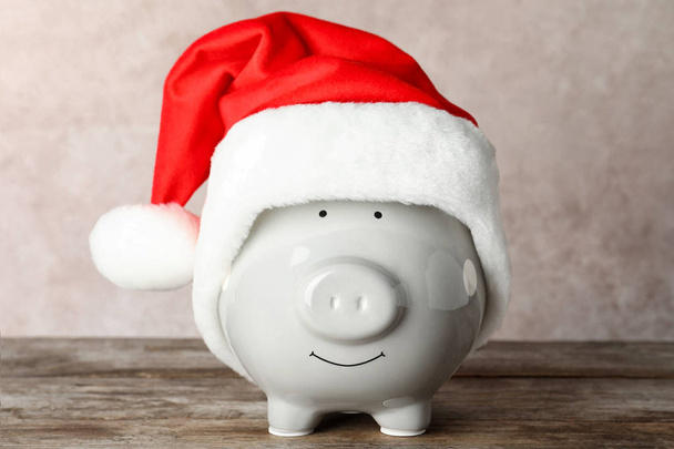 Cute piggy bank with Santa hat on table - Fotó, kép