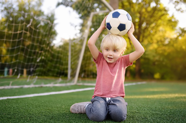 Little boy having fun playing a soccer/football game on summer day. Active outdoors game/sport for children. Kids soccer classes and camps - 写真・画像