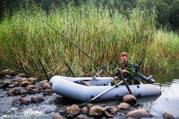 Man in camouflage fishing rod on the river on a rubber boat. - Photo, Image