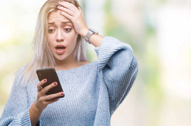 Young blonde woman texting sending message using smartphone over isolated background stressed with hand on head, shocked with shame and surprise face, angry and frustrated. Fear and upset for mistake. - Foto, imagen