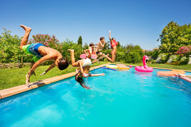 Side view shot of teenage boys and girls, happy friends, doing front flip together in swimming pool - Foto, Bild