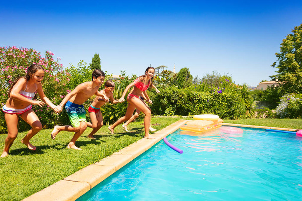 Group of teenage boys and girls in swimwear holding hands, running together to swimming pool - Photo, image