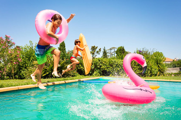 Portrait of age-diverse boys and girls, happy friends, jumping in water with inflatable swim floats, enjoying pool party in summer - Foto, imagen