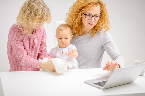 pracowita matka za pomocą laptopa, podczas gdy jej dzieci bawiące się puszysty kotek - Zdjęcie, obraz