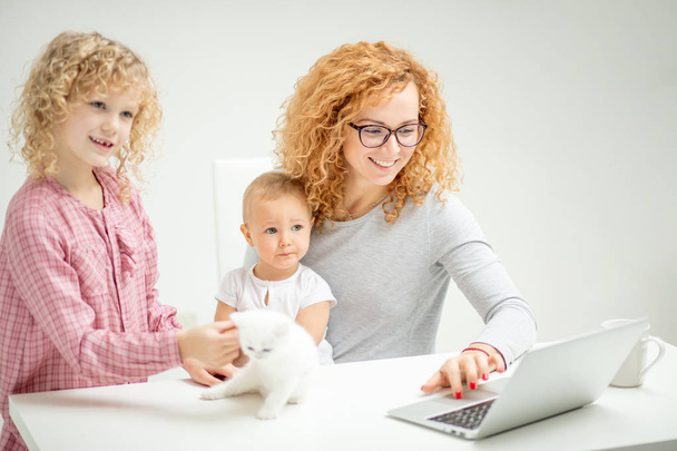 awesome positive red-haired girl browsing the Net with her little children - Foto, Bild