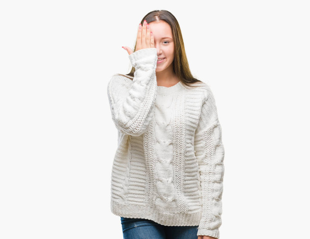 Young beautiful caucasian woman wearing winter sweater over isolated background covering one eye with hand with confident smile on face and surprise emotion. - Foto, immagini