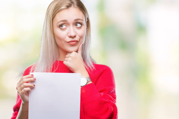 Молодая блондинка держит чистый лист бумаги на изолированном фоне серьезное лицо, думая о вопросе, очень запутанная идея
 - Фото, изображение