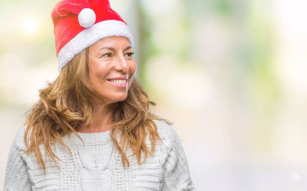 Mulher hispânica de meia idade usando chapéu de Natal sobre fundo isolado olhando para o lado com sorriso no rosto, expressão natural. Rindo confiante
. - Foto, Imagem