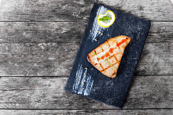 Baked salmon fillets with red caviar and lemon on stone slate background close up. Healthy food - Photo, image
