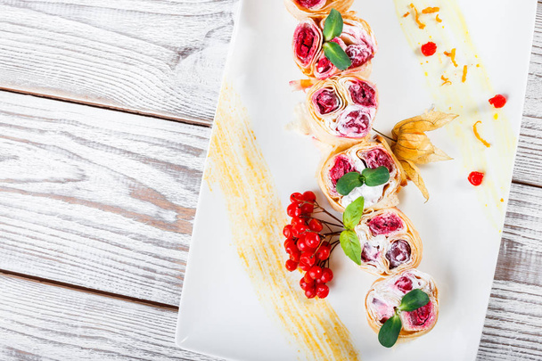 Pancakes with cream cheese, cherries decorated by berries and physalis on light wooden background close up. Traditional Russian cuisine. Sweet dessert. Flat lay. Top view - 写真・画像