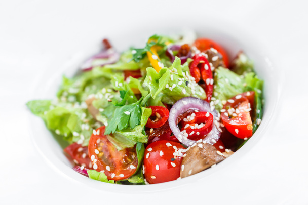 Fresh vegetable salad with lettuce, grilled mushrooms, tomatoes, sweet peppers and sesame seeds on plate on light wooden background close up. Healthy food. Top view - Photo, Image