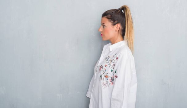 Mladé dospělé ženy přes zeď grunge šedou košili květy při pohledu na stranu, uvolnit profilu pozice s přirozenou tvář s sebejistý úsměv. - Fotografie, Obrázek