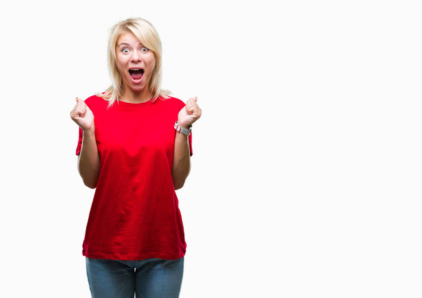 Joven mujer rubia hermosa vistiendo camiseta roja sobre fondo aislado celebrando sorprendido y sorprendido por el éxito con los brazos levantados y los ojos abiertos. Concepto ganador
. - Foto, imagen