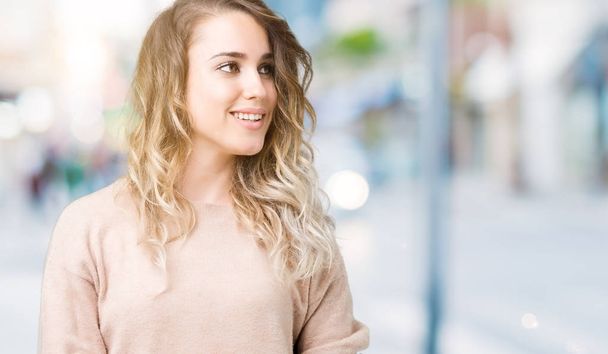 schöne junge blonde Frau mit Sweatshirt über isoliertem Hintergrund, die mit einem Lächeln im Gesicht und natürlichem Ausdruck zur Seite schaut. Lachen selbstbewusst. - Foto, Bild