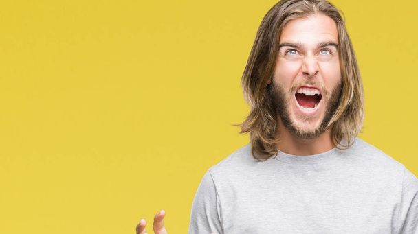 Young handsome man with long hair over isolated background crazy and mad shouting and yelling with aggressive expression and arms raised. Frustration concept. - Foto, Imagem