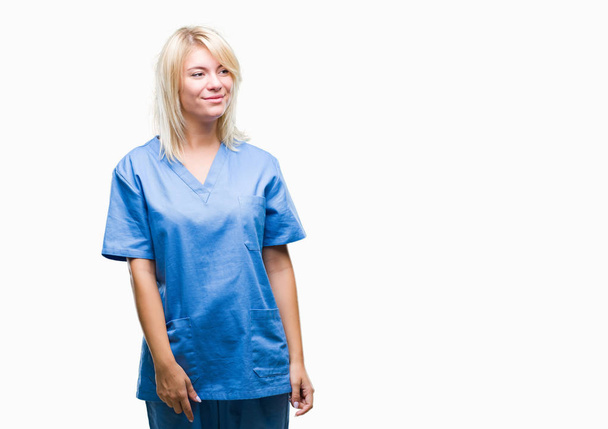 Young beautiful blonde nurse doctor woman over isolated background looking away to side with smile on face, natural expression. Laughing confident. - Φωτογραφία, εικόνα