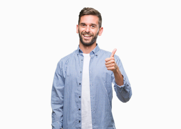 Mladý pohledný muž na sobě bílé tričko izolované pozadí dělá šťastné palec nahoru gesto rukou. Schvalování výraz s ukazuje úspěch při pohledu na fotoaparát. - Fotografie, Obrázek
