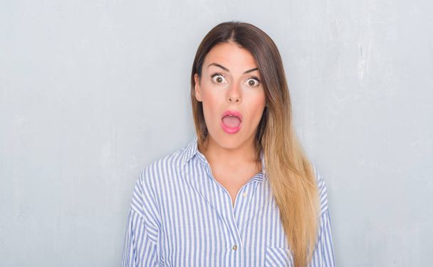 Young adult woman over grunge grey wall wearing business shirt afraid and shocked with surprise expression, fear and excited face. - Foto, immagini