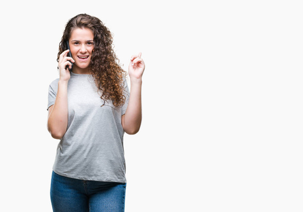 Giovane ragazza bruna che parla su smartphone su sfondo isolato sorpreso da un'idea o una domanda che punta il dito con la faccia felice, numero uno
 - Foto, immagini