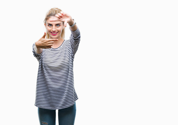 Young beautiful blonde woman wearing stripes sweater over isolated background smiling making frame with hands and fingers with happy face. Creativity and photography concept. - Foto, Imagen