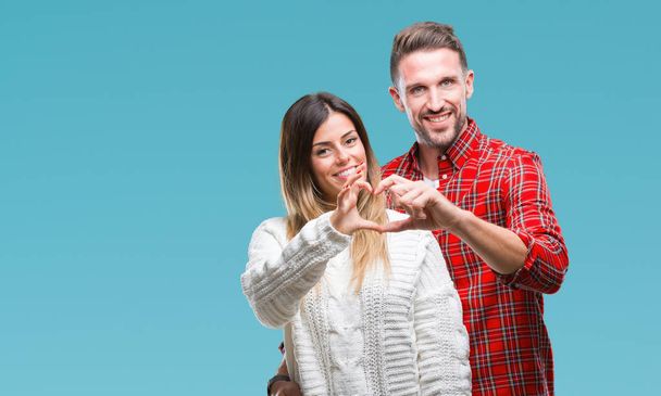 Young couple in love wearing winter sweater over isolated background smiling in love showing heart symbol and shape with hands. Romantic concept. - Photo, Image