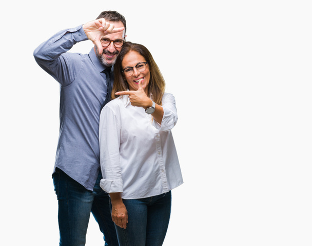 Middle age hispanic couple in love wearing glasses over isolated background smiling making frame with hands and fingers with happy face. Creativity and photography concept. - Photo, Image