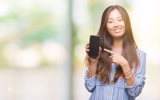 Jonge Aziatische vrouw weergegeven: leeg scherm van de smartphone over geïsoleerde achtergrond erg blij met de hand en de vinger te wijzen - Foto, afbeelding