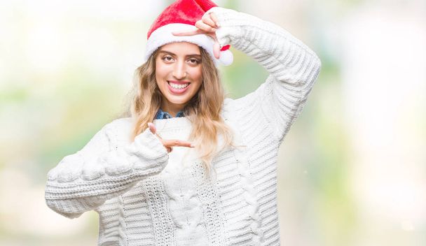 Belle jeune femme blonde portant un chapeau de Noël sur fond isolé souriant faisant cadre avec les mains et les doigts avec le visage heureux. Concept de créativité et de photographie
. - Photo, image