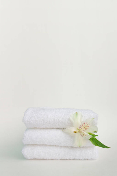 Beautiful alstroemeria flower and stack of three clean white spa salon bath towels isolated on white background. Front view copy space close up - 写真・画像
