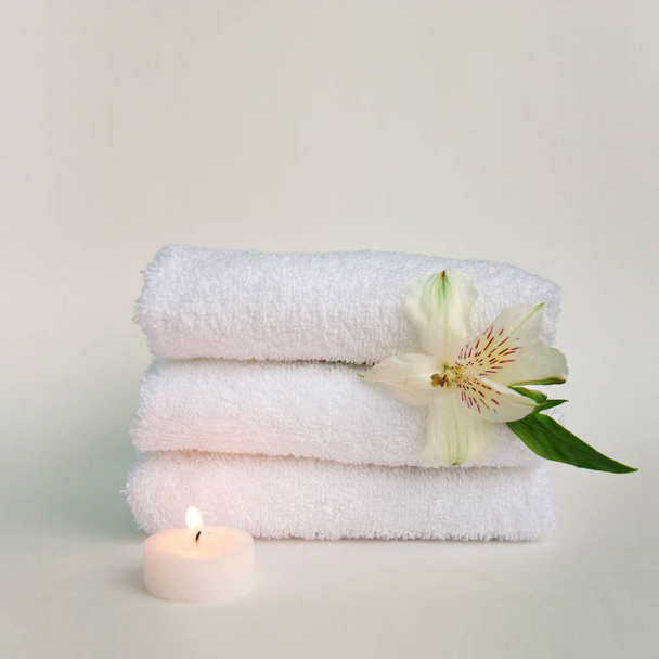 Beautiful alstroemeria flower, burning candle and stack of three clean white spa salon bath towels isolated on white background. Front view copy space close up - Foto, Imagem