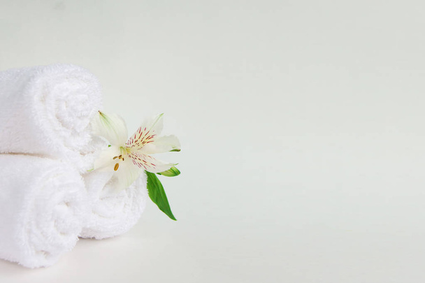 Alstroemeria flower and three rolls of clean white spa salon bath towels isolated on white background. Front view copy space close up - Photo, image