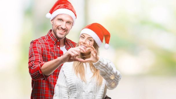 愛恋ハートマークと手で形を示す笑みを浮かべて分離の背景にクリスマスの帽子をかぶっての若いカップル。ロマンチックな概念. - 写真・画像