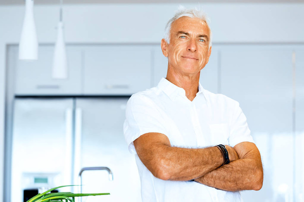 Portret van een slimme senior man permanent in keuken - Foto, afbeelding