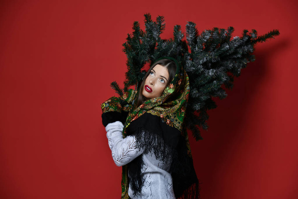 Happy Russian style woman with scarf hold Christmas  tree on her shoulders happy laughing  - Foto, afbeelding