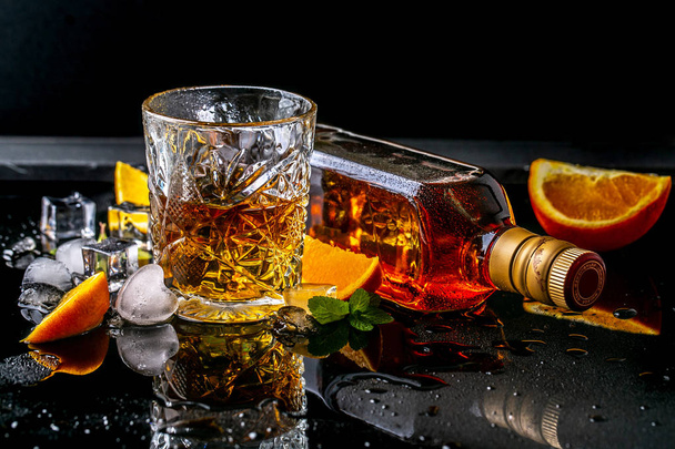 ウイスキーと高価なウイスキーのボトルの男性的なリラクゼーションガラスのためのエリートドリンク、黒の反射背景の氷、コピースペース. - 写真・画像