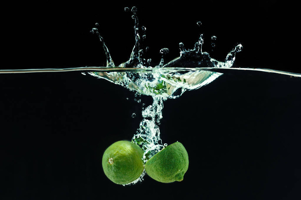 Fresh limes dropped into water with splash - 写真・画像