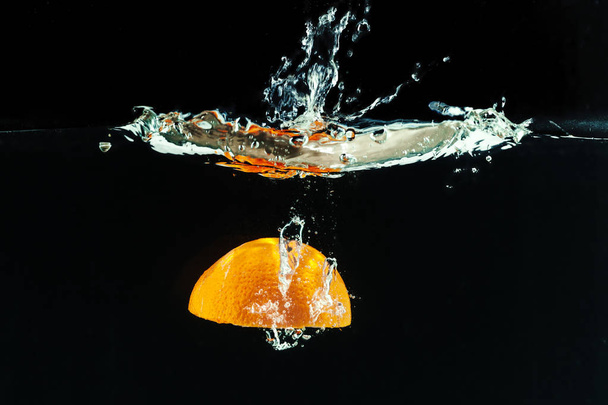 Orange falling into the water and making splashes  against black background  - Photo, Image