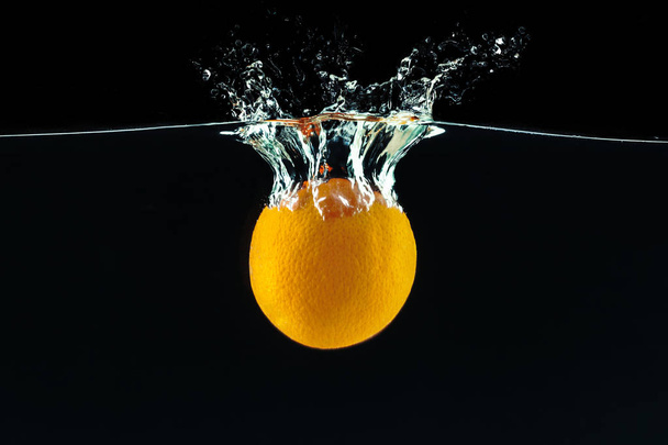Orange falling into the water and making splashes  against black background  - Фото, изображение