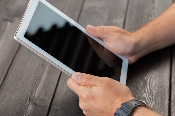 hands of a man holding tablet device over a wooden workspace table - Photo, image