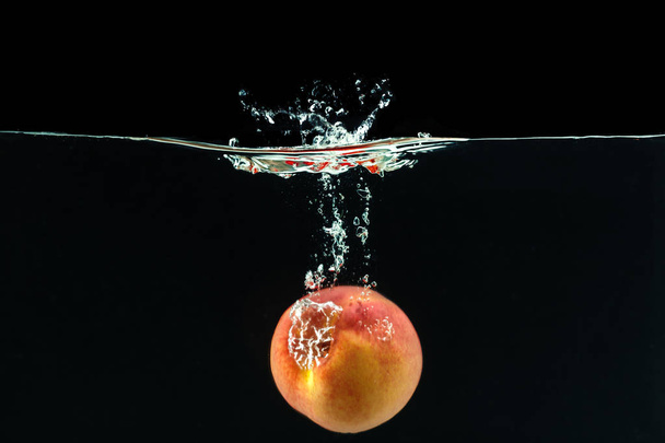 Peach dropped into water with bubbles - Φωτογραφία, εικόνα
