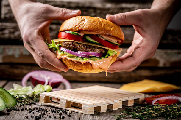 Detailní záběr rukou drží doma z chutného hamburgeru na dřevěném vinobraní stolu. - Fotografie, Obrázek