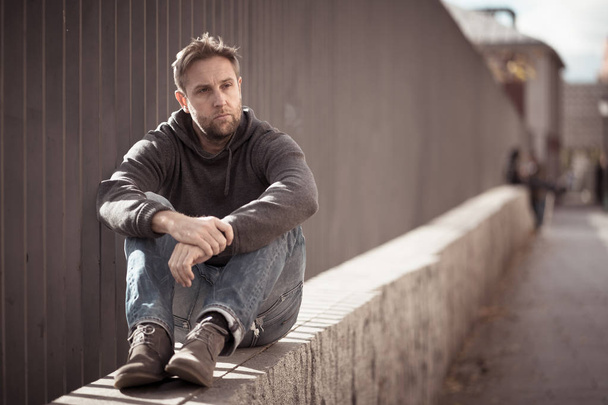 Young attractive man suffering from depression stress sitting alone and sad on the street feeling anxious and lonely in unemployment Mental health Drug and alcohol addiction concept. - Фото, зображення